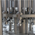 Close-up image of an industrial machine with multiple metal pipes and connectors. The equipment features a complex arrangement of cylindrical components, valves, and tubing, suggesting it is designed for tasks such as bottling or filling in a manufacturing process.