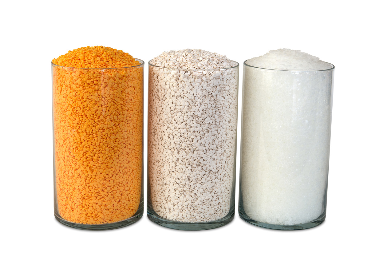 Three transparent glass cylinders are filled to the brim with granular substances: the leftmost contains orange lentils, the middle holds white rice, and the rightmost is filled with white sugar. They are arranged in a row against a plain white background.
