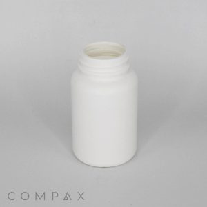 A small white plastic bottle with a screw-on cap sits on a light grey surface. The bottle is empty and open, with the cap removed. The brand name "COMPAX" is visible in the bottom left corner of the image.