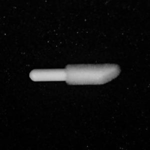 A white Nylon Flocking Applicator is centered against a black background in this image. The left end of the applicator is cylindrical and rounded, while the right end is tapered and pointed. The image appears grainy and slightly blurred.