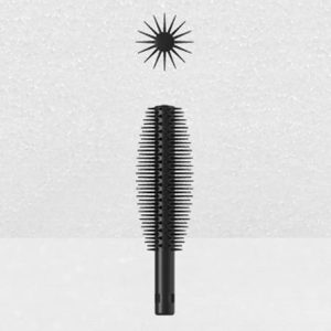 A Plastic Brush Applicator with fine, evenly spaced bristles stands vertically against a light grey background. Above the applicator is a spiky, star-like graphic element.
