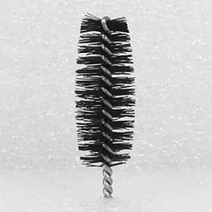 A close-up image shows the Nylon Brush Applicator, a small cylindrical wire brush with tightly packed, stiff bristles. The bristles are arranged in a spiral pattern around a twisted wire core. The background is uniformly textured and white.