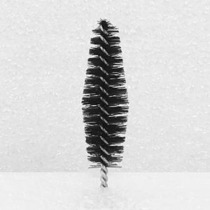 A close-up view of the Nylon Brush Applicator, featuring dense and evenly spaced bristles resembling those of a small bottle brush, set against a plain white background. The brush has a black color and a twisted metal handle.