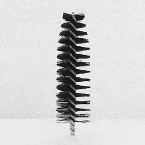 A black and white image of a Nylon Brush Applicator with stiff bristles extending outward in all directions. The handle is a twisted wire. The background features a speckled textured surface.