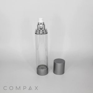 A clear, cylindrical spray bottle with silver accents, featuring a spray nozzle on top and an additional silver cap beside it on a light gray background. The word "COMPAX" is visible at the bottom left corner of the image.