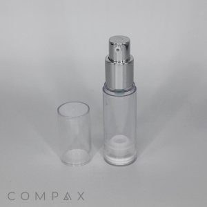 A transparent, cylindrical spray bottle with a silver nozzle and a clear, removable cap placed beside it. The word "COMPAX" is visible at the bottom left corner of the image.