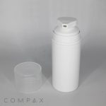 A white cylindrical pump dispenser with a clear cap placed beside it. The dispenser has a small rectangular nozzle on its top. The background is plain and light gray. The word "COMPAX" is written at the bottom left corner.