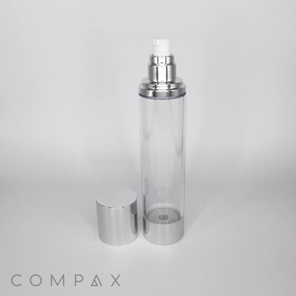 A transparent, cylindrical bottle with a silver pump top and a matching removable cap displayed beside it. The bottle sits on a clean, white surface with the brand name "COMPAX" visible in the bottom left corner.