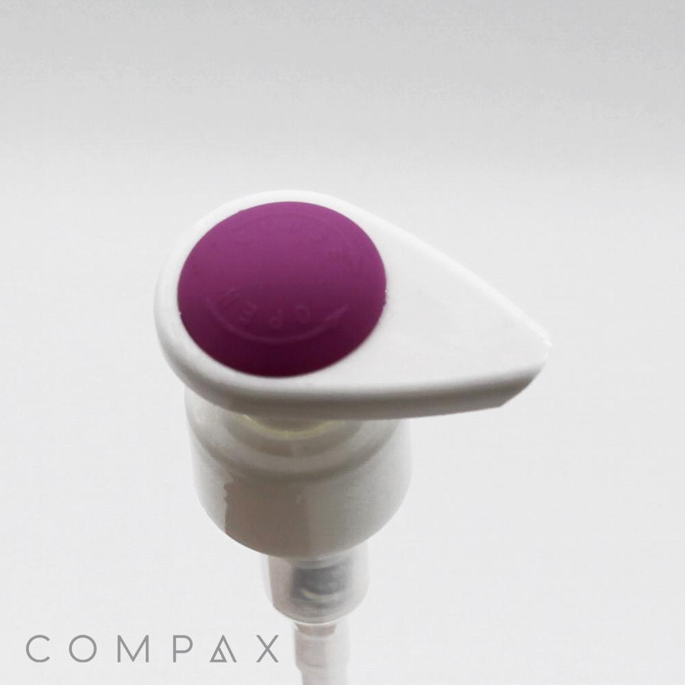 A white plastic pump dispenser with a silicone top in purple is set against a plain white background. The branding text "COMPAX" is partially visible in the bottom left corner.