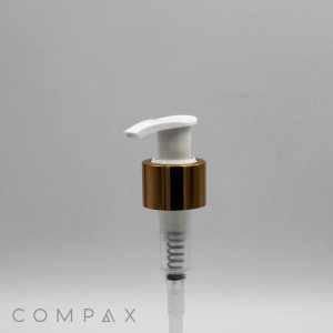 A white plastic pump with a shiny gold collar and a clear tube underneath is displayed against a plain, light gray background. The brand name "COMPAX" is visible at the bottom left corner.