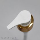 Top view of the Pump, featuring a white dispenser pump atop a gold bottle, placed on a reflective gray surface. The pump handle is angled diagonally to the left. The brand name "COMPAX" is visible in gray text at the bottom left corner.