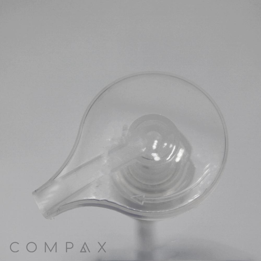 A close-up of the Large Teardrop Pump, a transparent, circular plastic object with a small curved nozzle on one side, viewed from above against a grey background. The word "COMPAX" is written in light grey capital letters in the bottom left corner.