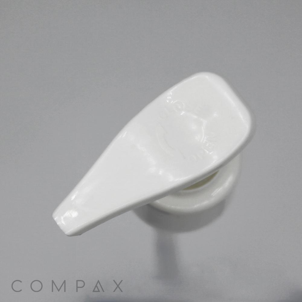Close-up image of the Pump, a white plastic lotion dispenser with a curved nozzle and a rectangular top, set against a light gray background. The word "COMPAX" is printed in gray at the bottom left corner of the image.