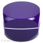 A shiny, round, purple cosmetic container with a smooth, seamless design. The container has a glossy finish and a slight reflection on its surface, indicating a polished look. The brand name "COMPAX" is subtly visible in the lower left corner.