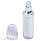 A sleek, transparent spray bottle, named the Double Wall Airless Bottle, with silver accents and a cylindrical shape, showcased with its clear cap removed and placed beside it. The bottle's top features a silver pump dispenser for easy application. The word "COMPAX" is visible in the lower-left corner.