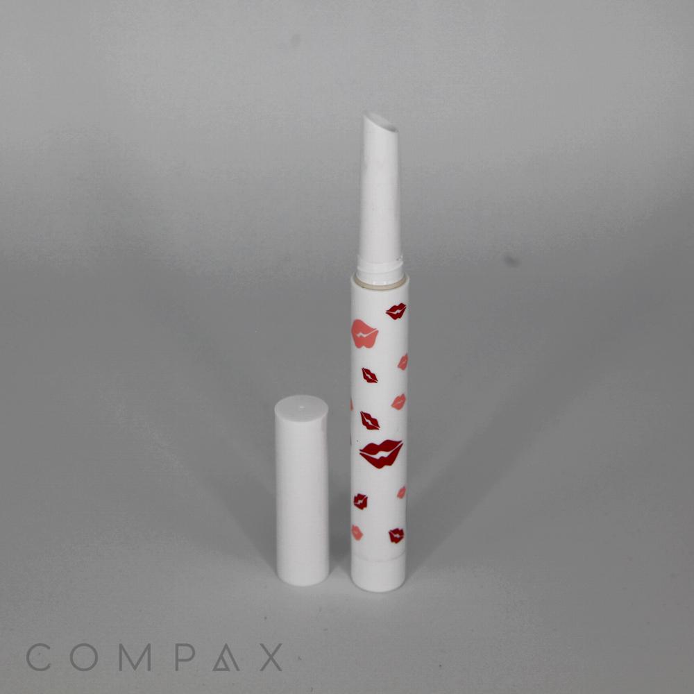 A white cylindrical lip balm container decorated with red lipstick kiss marks, standing upright on a plain background. The cap is removed and placed beside it. The word "COMPAX" is marked on the bottom-left corner of the image.