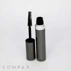 A sleek, gray mascara tube with the cap removed, revealing a black mascara wand. The wand is positioned upright and coated with black mascara. The brand name "COMPAX" is visible at the bottom of the image. The background is plain white.