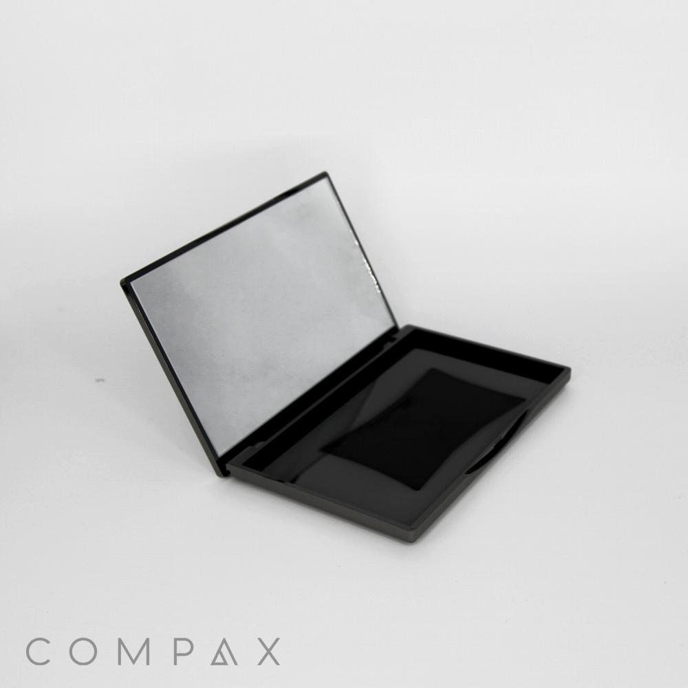 A sleek, empty Rectangular Compact with Mirror is shown open, revealing its reflective upper lid and a plain, unfilled bottom compartment. The word "COMPAX" appears at the bottom left corner on a white background.