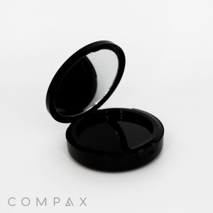 A sleek Single Well Round Compact with Mirror in black, featuring an open lid that reveals a mirror inside the top cover. The compact appears empty, with the word "COMPAX" visible in light gray text at the bottom left corner of the image.