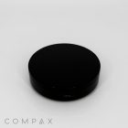 A round, black Single Well Round Compact with Mirror is displayed against a white background. The compact is closed, showcasing a smooth, matte finish. The brand name "COMPAX" appears in grey text at the bottom left corner of the image.