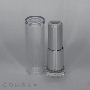 A sleek, silver tube of the Round Textured Lipstick stands upright next to its transparent cap. The brand name "COMPAX" is visible at the bottom-left corner of the image. The modern design features a minimalist aesthetic against a plain, light background.