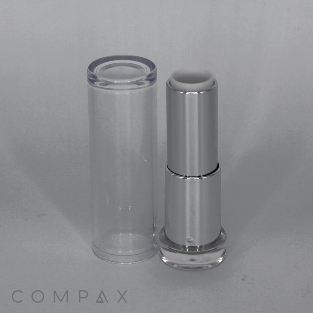 A sleek, silver tube of the Round Textured Lipstick stands upright next to its transparent cap. The brand name "COMPAX" is visible at the bottom-left corner of the image. The modern design features a minimalist aesthetic against a plain, light background.