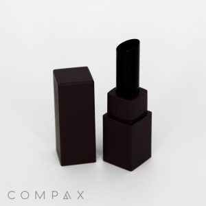 A black Square Lipstick tube, with the cap removed, stands upright on a white background. The words "COMPAX" are visible in the bottom left corner.