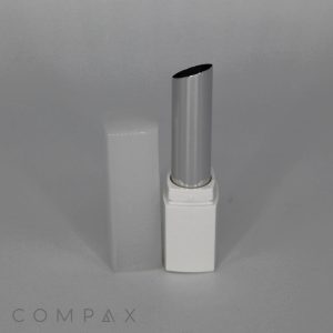 A Square Slimline Lipstick in a white rectangular case with the cap removed, revealing the angled tip of the lipstick. The cap is placed next to the case. The word "COMPAX" is visible in the bottom left corner of the image.