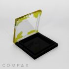 A Single Well Square Compact with a hinged lid, featuring yellow edges and a transparent plastic design. The lid is partially open, revealing an empty black interior. The word "COMPAX" is printed in gray at the bottom left corner of the image.