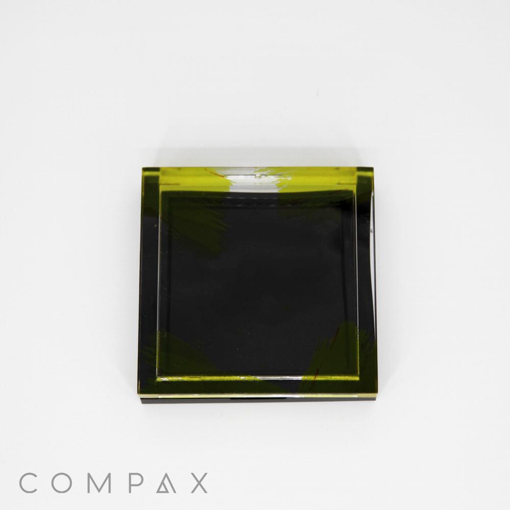 A Single Well Square Compact mirror with a black and yellow-green translucent design is displayed on a white background. The word "COMPAX" is printed in gray at the bottom left corner.