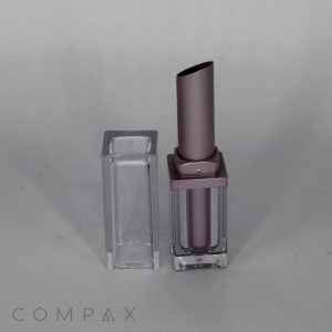 A minimalist photo showcasing the Square Heavy Wall Lipstick in a sophisticated metallic purple case. The lipstick stands upright with the cap removed and placed beside it, while the brand name "COMPAX" is subtly displayed in the bottom left corner against a neutral background.