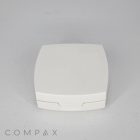 A white, square "Square Cushion Compact" case with a subtly curved lid is centered against a plain background. The brand name "COMPAX" is visible in light gray text at the bottom left corner of the image.