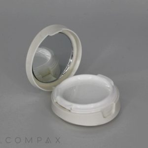 A small, round "Round Cushion Compact with Mirror" features an open compact case with a mirror on the lid and an empty compartment in the base. The compact is white and is set against a plain, light gray background. The brand name "COMPAX" is visible in the lower-left corner.