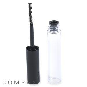 A clear empty Round Mascara Bottle and a black mascara brush with its wand are placed side by side. The brand name "COMPAX" is printed at the bottom of the image. The black brush handle stands vertically inside the open tube cap.