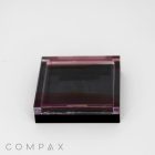 A Single Well Square Compact, transparent with a slight tint, closed shut. It features sleek and minimalist packaging with a subtle black gradient. The brand name 'COMPAX' is written in light gray letters at the bottom left corner of the image on a white background.