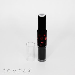 A Round Dual Beauty Stick with a transparent cap stands upright. The black tube features a pattern of red lips and contains white product. The brand name "COMPAX" is visible in gray text at the lower left corner of the white background.