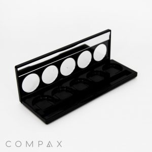 An open "5 Well Rectangular Compact with Windows" makeup palette in black, featuring five empty circular slots for powders or eyeshadows, and a mirror along the inside of the lid. The brand name "COMPAX" is printed in light gray at the bottom left corner of the image.