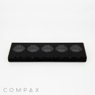 A sleek black 5 Well Rectangular Compact with Windows features five circular compartments arranged in a horizontal row. The brand name "COMPAX" is displayed in small, gray text at the bottom left corner of the image, set against a plain white background.