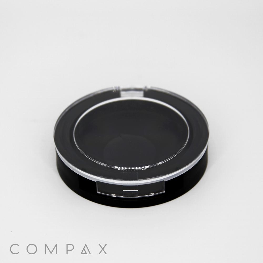 A Single Well Round Compact case, featuring a black base and a transparent lid, sits on a plain white background. The word "COMPAX" is printed in gray text in the bottom left corner of the image.