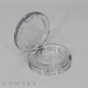 A Single Well Round Compact cosmetic case is open with its lid tilted back, revealing the inner compartment designed for makeup. The background is plain white, and the brand name "COMPAX" is visible at the bottom left.