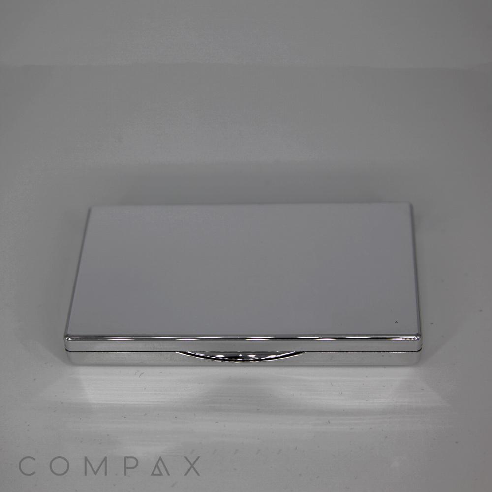 A sleek, silver 3 Well Rectangular Compact case with rounded edges. The case is closed and has a smooth, reflective surface. The word "COMPAX" is faintly visible at the bottom of the image.