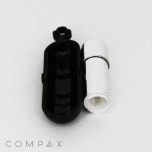 A black compact container with one open lid and an empty, round compartment beside a white cylindrical Bullet Lipstick. The word "COMPAX" is written in light gray capital letters at the bottom left corner. The background is plain white.