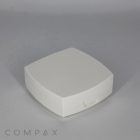 A small, white Square Cushion Compact with rounded edges and a small latch at the front. The background is a plain, light gray surface. The word "COMPAX" appears in the bottom left corner.