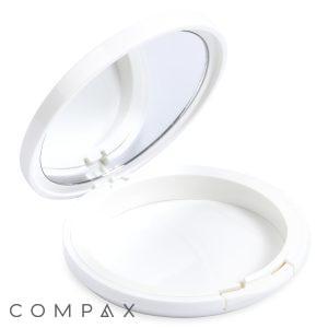 A round white Single Well Round Compact with Mirror is shown with its lid open. Inside the top lid, there's a mirror. The bottom part of the case is empty, and the brand name "COMPAX" is printed in gray letters at the bottom left corner of the image.