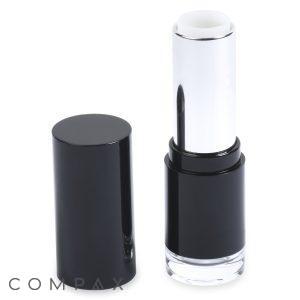 An open black and silver tube of Round Lipstick with the cap placed next to it. The tube is displaying a white or colorless lipstick. The brand name "COMPAX" is visible in gray letters at the bottom left corner of the image.