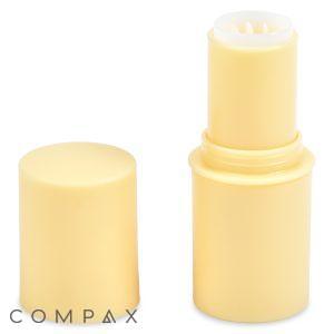 A yellow, cylindrical Mini Stick twist-up container with its cap removed, revealing the product inside. The cap is standing upright next to the container. The brand name "COMPAX" is positioned at the bottom left corner of the image.