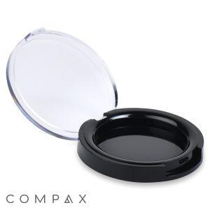 A Round Compact featuring a black, open design with a clear lid. Inside, the bottom of the case is divided into two deep and narrow sections, separated by a flat surface in the center. Positioned against a white background, the compact prominently displays the "COMPAX" brand name at the bottom left.