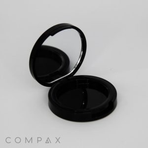An open black compact case with a mirror on the upper lid and an empty compartment on the bottom. The background is plain white, and the word "COMPAX" is written in the lower left corner.