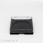 A black compact case with a clear lid, bearing the brand name "COMPAX" at the bottom left corner. The inside of the case is empty, displaying a circular recess likely meant to hold a cosmetic product. The image background is plain white.