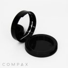 The image shows a black circular compact case with a mirror, open to display both the lid and the base. The interior is empty. The background is plain white, and the word "COMPAX" is visible in a stylish font at the bottom left corner.
